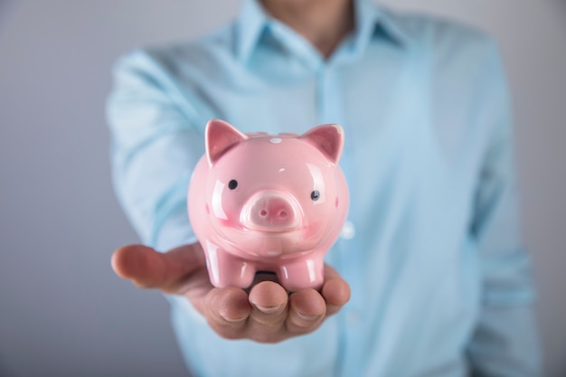 A man in a shirt holds a piggy bank in his hand