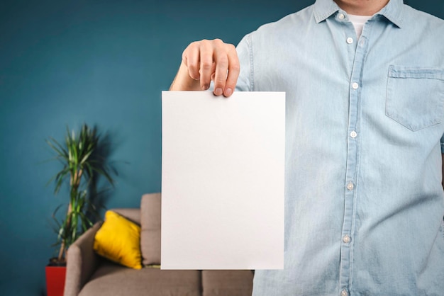 A man in a shirt is holding a white piece of paper at home