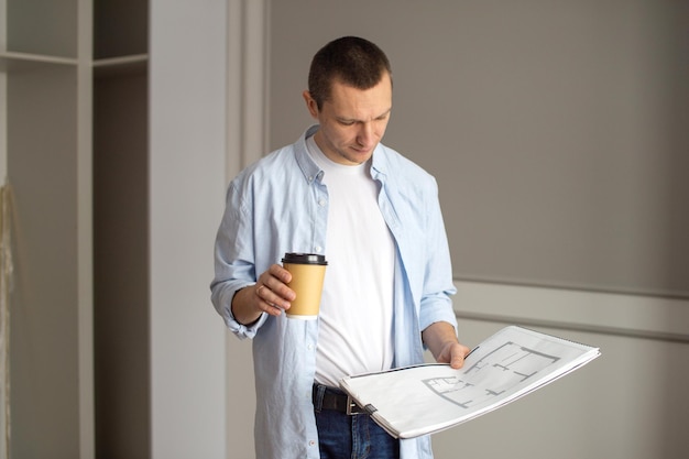 Photo a man in a shirt is looking at an album with drawings holding a disposable cup indoor repair work