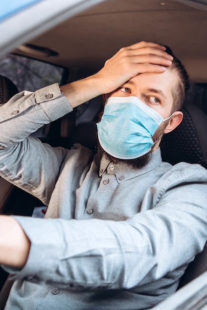 man in shirt and medical mask sits at the wheel of car.