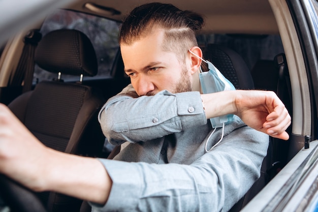 man in shirt and medical mask sits at the wheel of car.