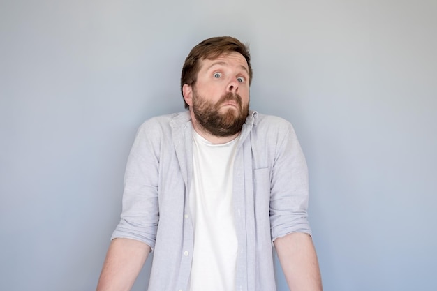 man in a shirt shrugs in surprise and looks at the camera with a strange and funny expression