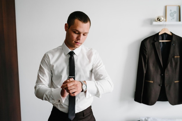 Photo a man in a shirt and tie adjusts the watch on his arm at home
