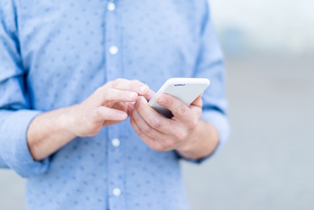 A man in a shirt uses a smartphone in the summer in the city.