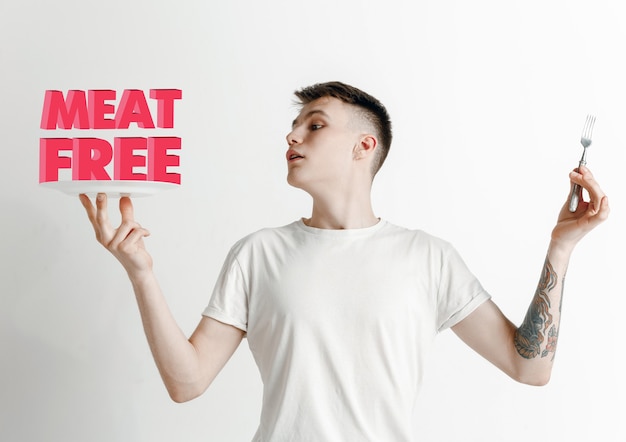 Man in shirt with the folk isolated on white. Male model holding a plate with letters of word Meat Free. Choosing healthy eating, diet, organic nutrition and nature friendy lifestyle.