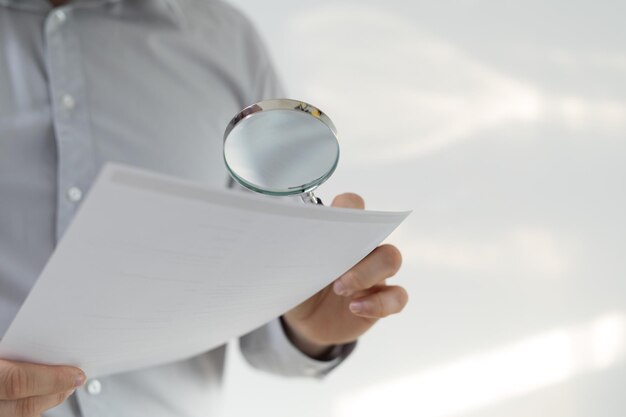 A man in a shirt with long sleeves looking at the papers through the magnifying glass