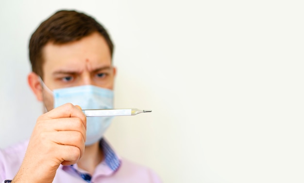 A man in a shirt with a mask on measures the temperature