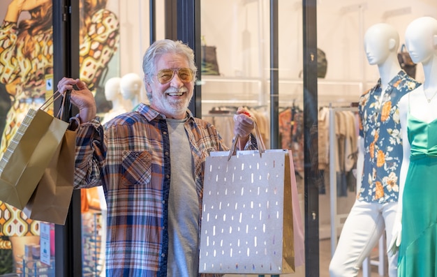 L'uomo nello shopping. uomo barbuto anziano spensierato con borse della spesa nel centro commerciale, concetto di consumismo