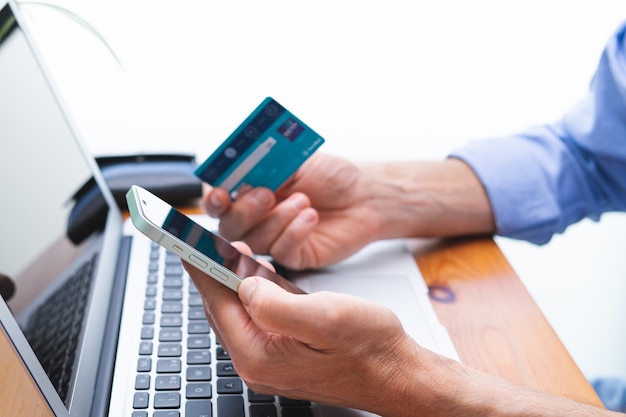 Man shopping and paying with cell phone and laptop and credit card. Copy space.