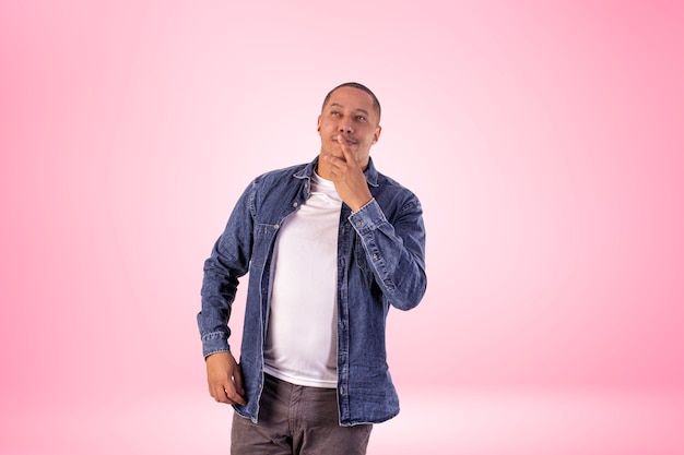 Man in short clothes wearing denim shirt, white t-shirt and brown pants in studio photo on a background with lights.