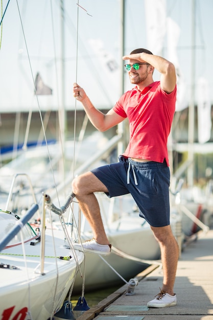 A man in shorts stands and holds on to a yacht.