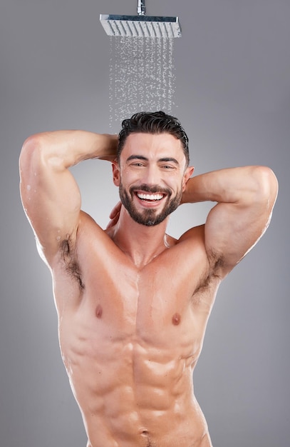 Man shower and cleaning in studio portrait by background smile and hygiene to start morning Model abdomen and happy with water drops wellness and healthy skincare process in bathroom for health