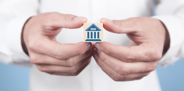 Man showing Bank symbol on wooden cube.