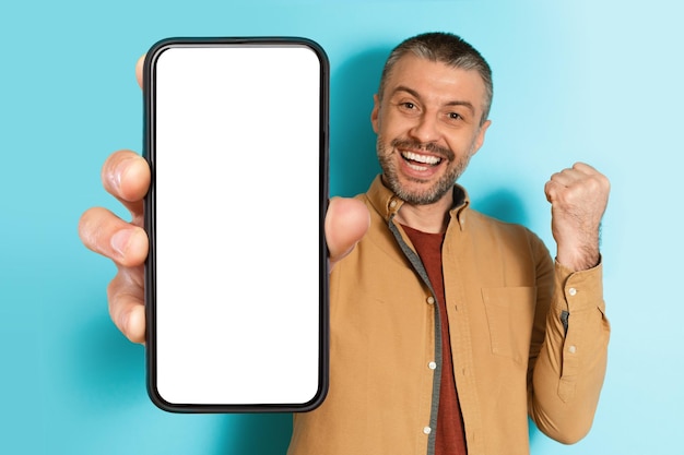 Мужчина показывает большой экран смартфона, жестикулируя "да" на синем фоне