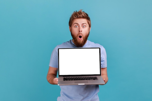 Man showing laptop with blank display place for your advertisement looking at camera with big eyes