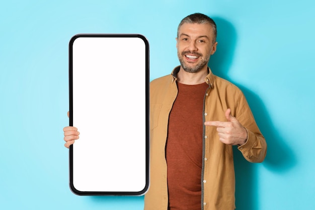 Мужчина показывает большое рекламное приложение для смартфона на макете синего фона