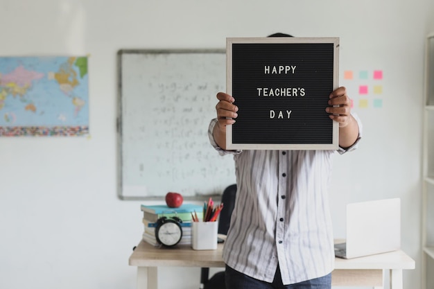 Photo a man showing lettering board with text happy teacher's day to the camera and standing inside moder