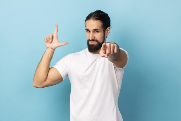 Photo man showing looser gesture and pointing at camera looking with grumpy face