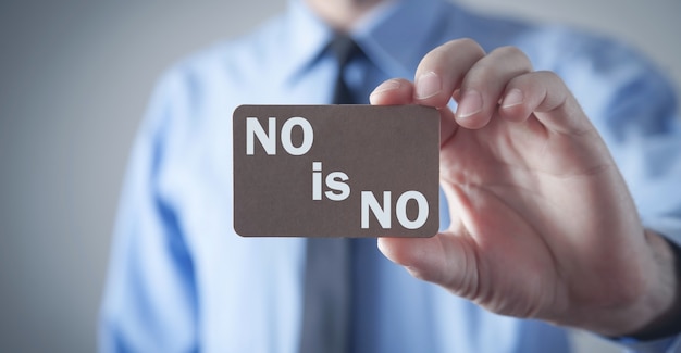 Man showing No Is No text on wooden board.