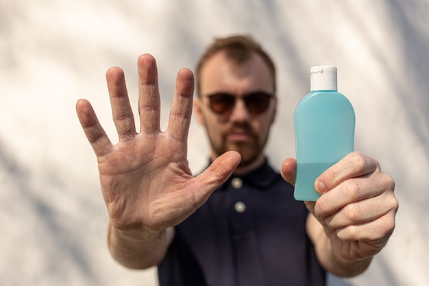 Man showing one hand and holding a bottle of antibacterial sanitizer