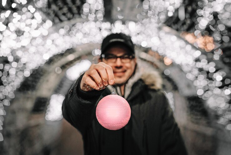 Photo man showing pink christmas bauble against christmas lights in the city