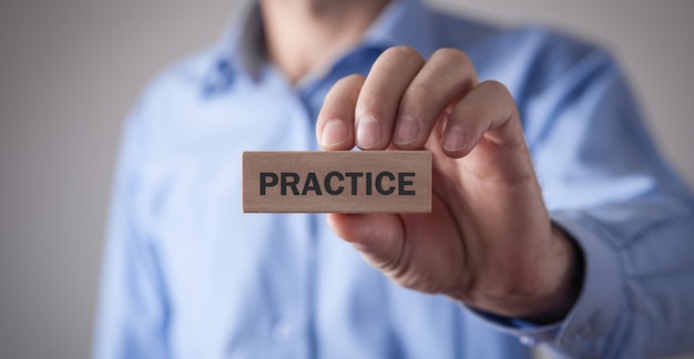 Man showing Practice word on wooden block.