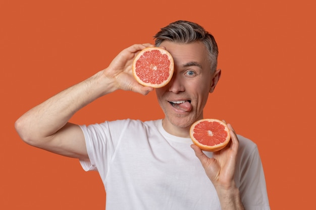 Man showing tongue holding halves of grapefruit