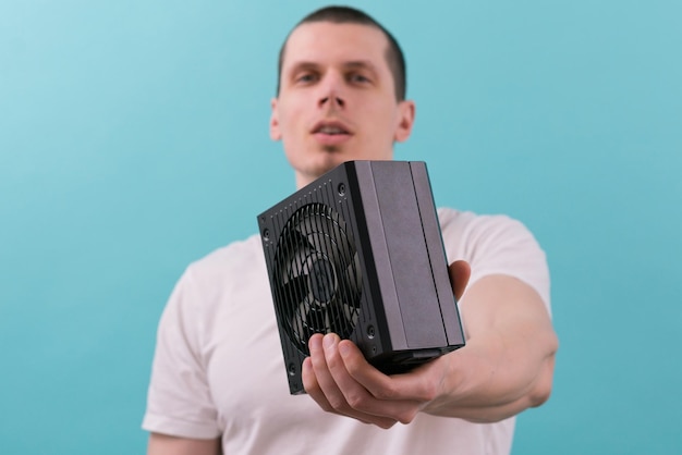 A man shows a computer power supply towards the camera on a\
blue background electric fan hightech ac element section watt\
ventilator personal computer tool distribution resource