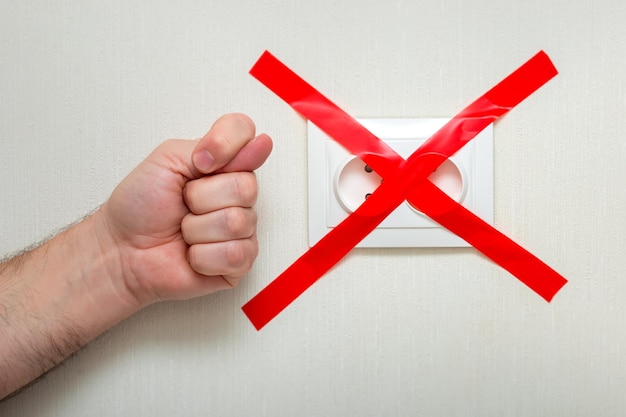 The man shows a fig gesture near the electrical outlet tied with a red ribbon criss-cross