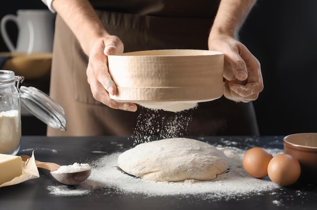 Man sifting flour over dough on table