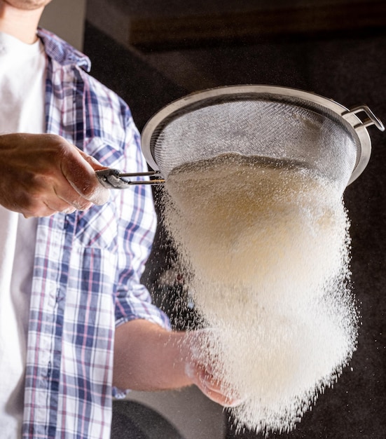 A man sifts flour through a sieve to make fresh bread Wheat flour of the highest grade for bread Flour aeration