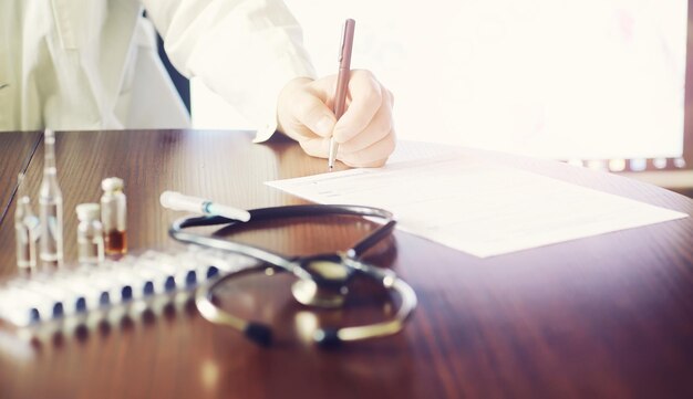 A man signs a medical document. Medical equipment on the table. Stethoscope and ampoules with syringes. Makes notes in the office. Medical center.