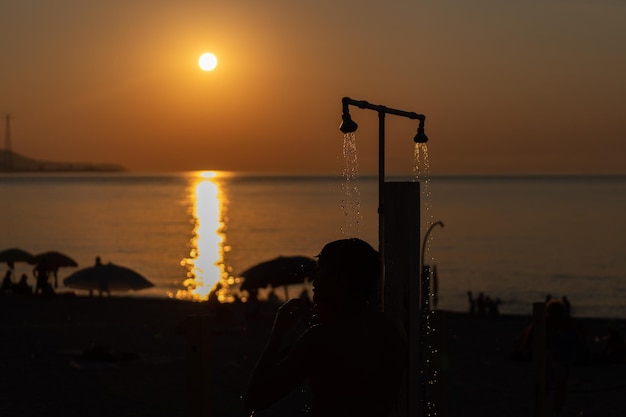 海のビーチで泳いだ後シャワーを浴びる男のシルエット オレンジ色の夕日の海の美しい景色 夏リゾート