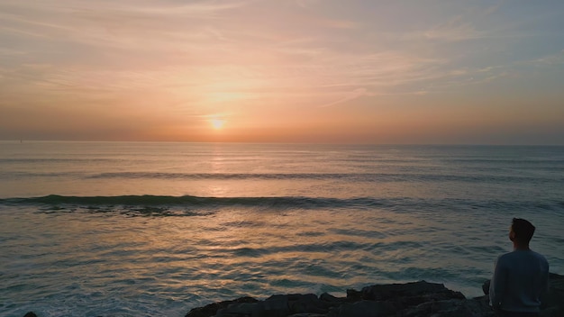 崖の後ろに夕日を見ている男のシルエットの無限の美しい海の地平線