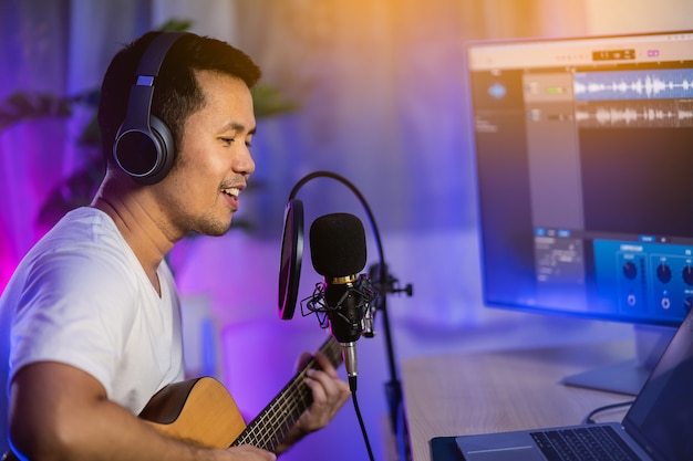 Man singing with headphone and playing guitar recording new song with microphone in the home recording studio