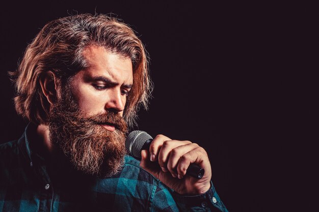 Man singing with microphone. Male singing with a microphones. Bearded man in karaoke sings a song into a microphone. Male attends karaoke. Man with a beard holding a microphone and singing