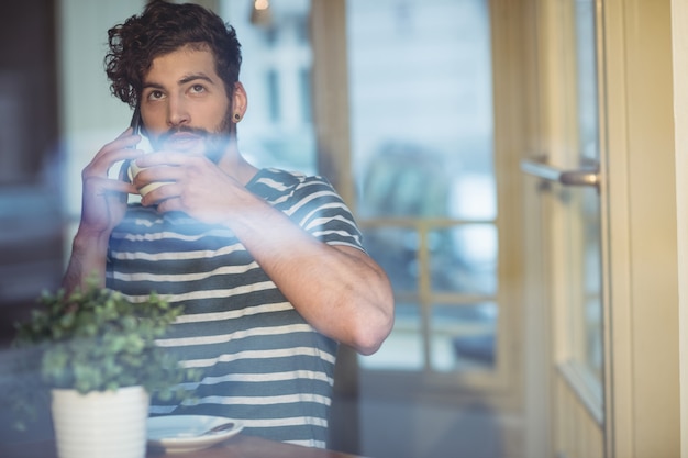 カフェで携帯電話で話しながらコーヒーをすすりながら男