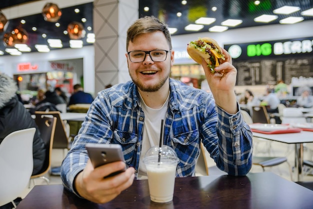 男はカフェに座ってハンバーガーを食べ、モバイルで見る