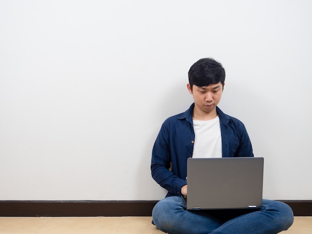 L'uomo si siede sul pavimento usando il laptop per lavorare da casa nella stanza