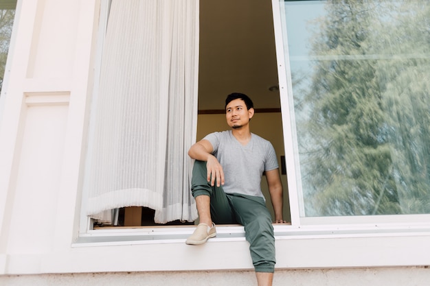 男は夏に家の正面玄関に座ってリラックスします。独身生活のコンセプトです。