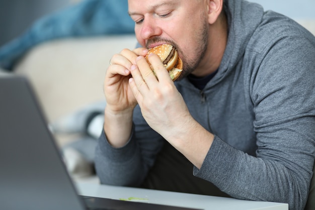 Man sit on sofa and eating burger against flat