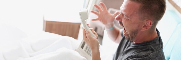 A man sits on the bed and shouts into the phone