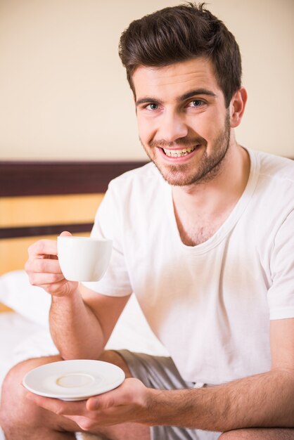 男は寝室に座って朝のコーヒーを飲みます。