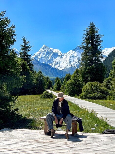 Photo a man sits on a bench in front of a snowy mountain.