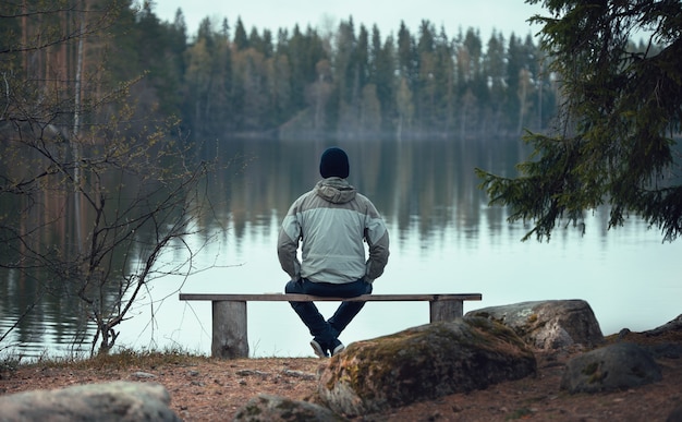 男は森の湖の近くのベンチに座っています。後ろからの眺め。