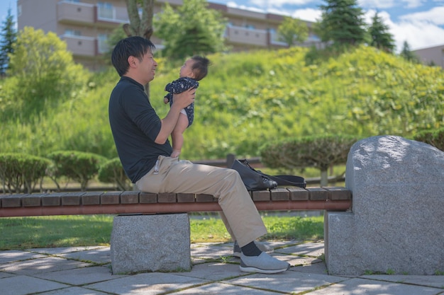 A man sits on a bench with his baby on his lap.