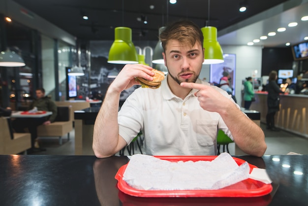 Foto l'uomo si siede in un bistrot e mostra una toppa su un hamburger tra le mani.