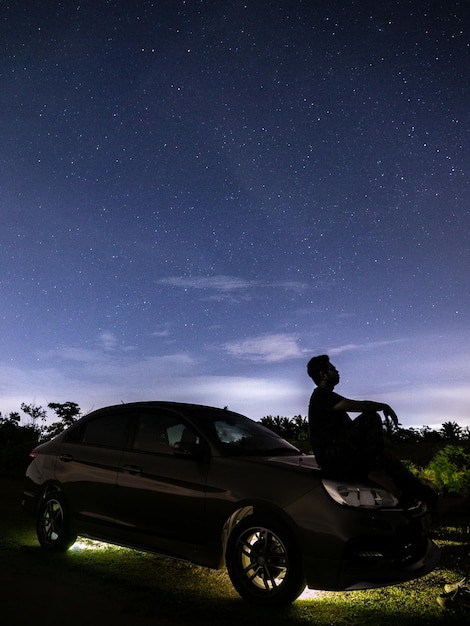 Foto un uomo siede su un'auto sotto un cielo stellato.