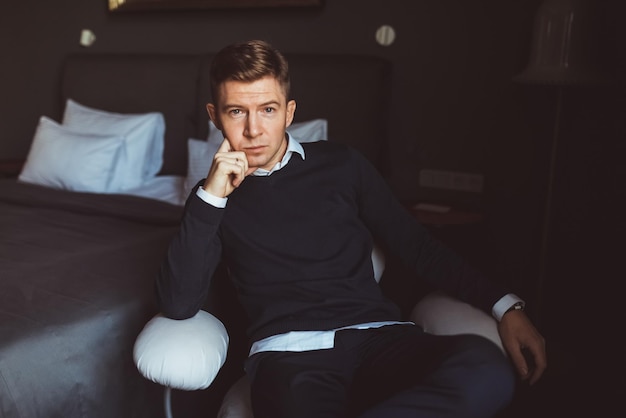 A man sits in a chair in a hotel room.