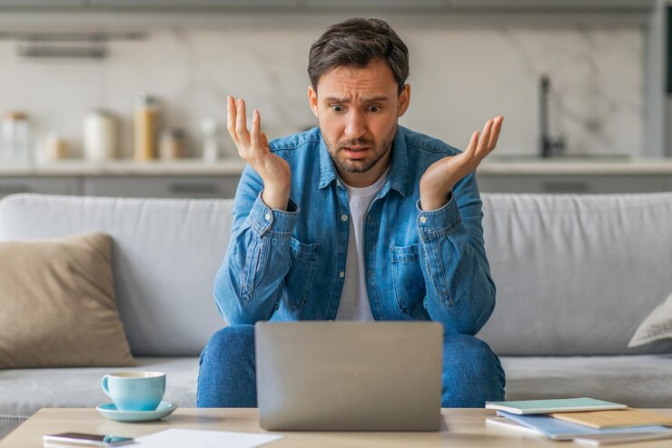 Photo a man sits on a couch in his living room looking confused as he stares at his laptop his arms are